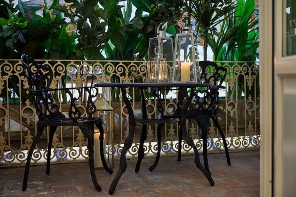 A patio with wrought iron furniture and candle-lit lanterns, surrounded by lush greenery.