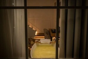 A hotel room with a large bed, a bedside table with a lamp, and a view of a staircase.