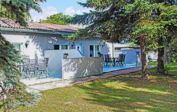 Une maison à deux étages avec un patio, un espace salon extérieur et un arbre au premier plan.