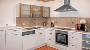 A kitchen with white cabinets, a stainless steel sink, a kettle, a coffee maker, and a toaster.