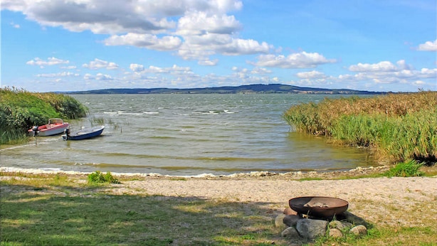 A calm river with boats, a sandy shore, and a distant mountain range under a partly cloudy sky.