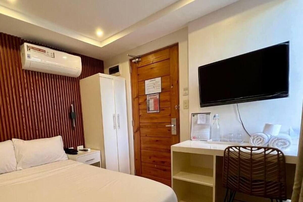 A hotel room with a bed, a desk, a television, and a wardrobe.