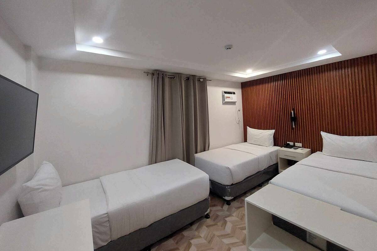 A hotel room with two single beds, a desk, a chair, a TV, and a wooden accent wall.