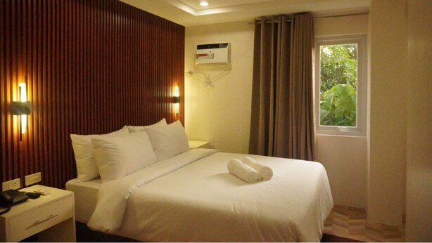 A hotel room with a bed, bedside table, lamp, air conditioning unit, window with curtains, and a view of greenery outside. - Casa Ison Hotel (Sablayan)