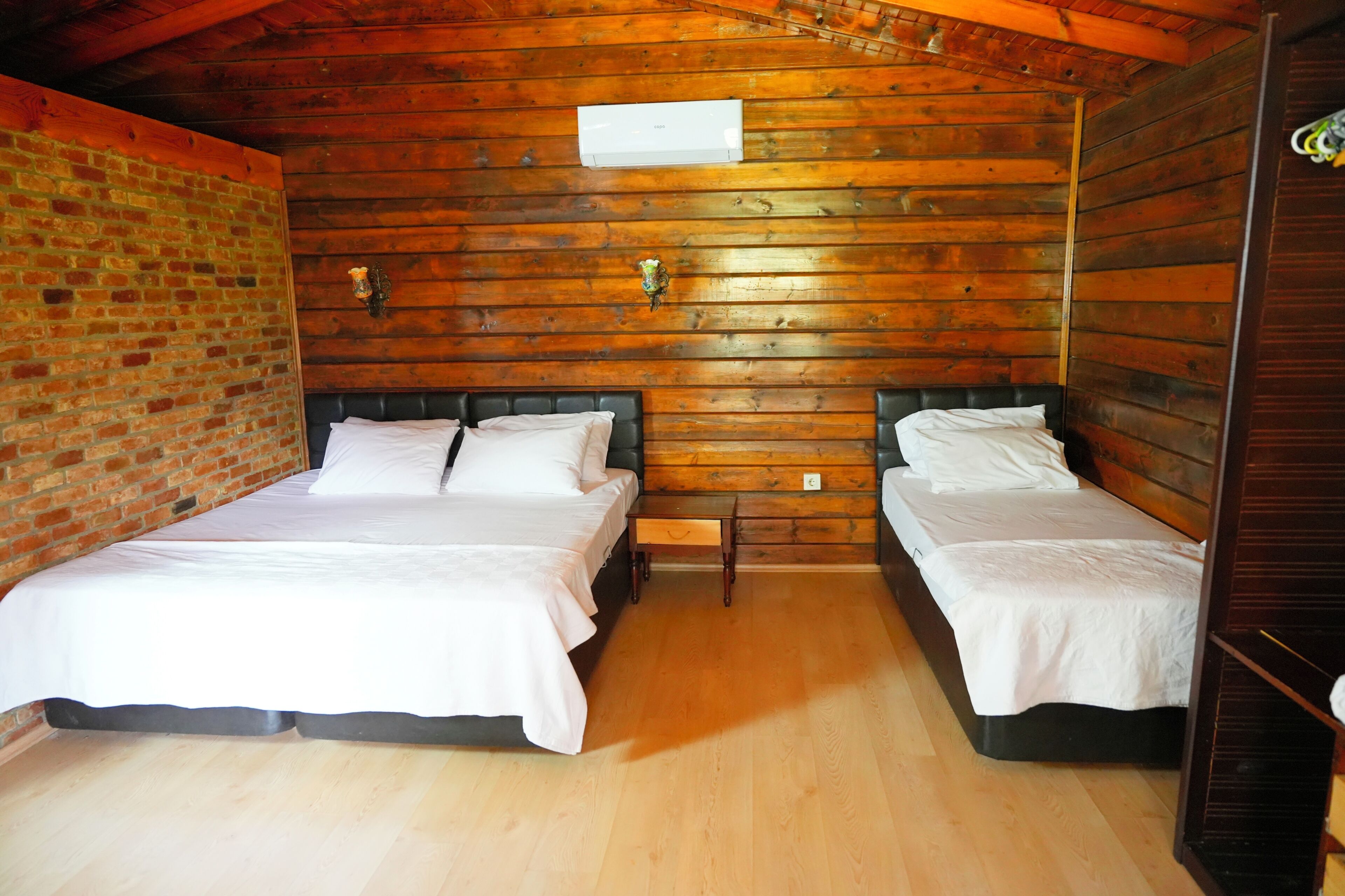 Una habitación con dos camas, paredes de madera, una pared de ladrillo y suelo de madera.