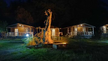 Un hotel de estilo cabaña con dos edificios principales, un árbol central y un pequeño muelle.