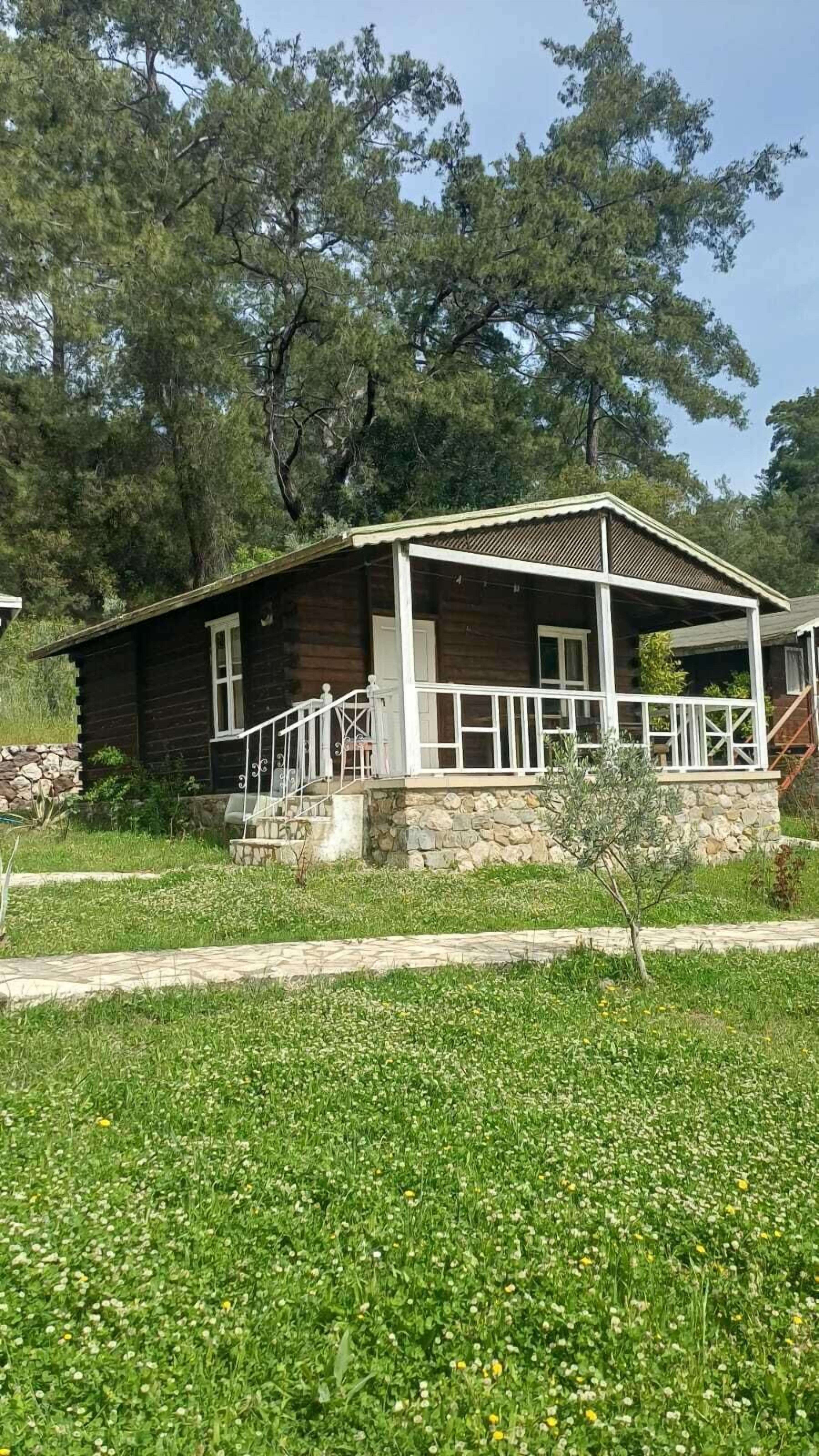 Una baita di legno con fondamenta in pietra, un portico con ringhiere bianche e un muro in pietra.
