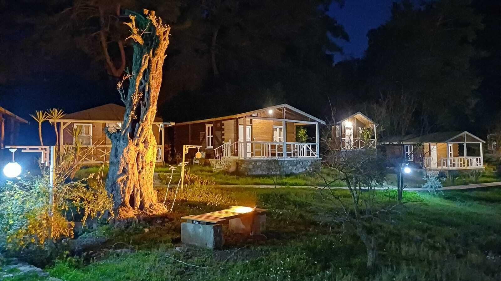 Une rangée de cabanes avec des fondations en pierre, des murs extérieurs en bois et une cour couverte d’herbe.