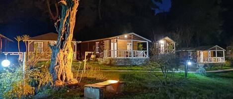 Une rangée de cabanes avec des fondations en pierre, des murs extérieurs en bois et une cour couverte d’herbe.
