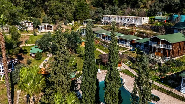 Oversigtsbillede af et resort med flere bygninger, en swimmingpool og frodigt grønt område.