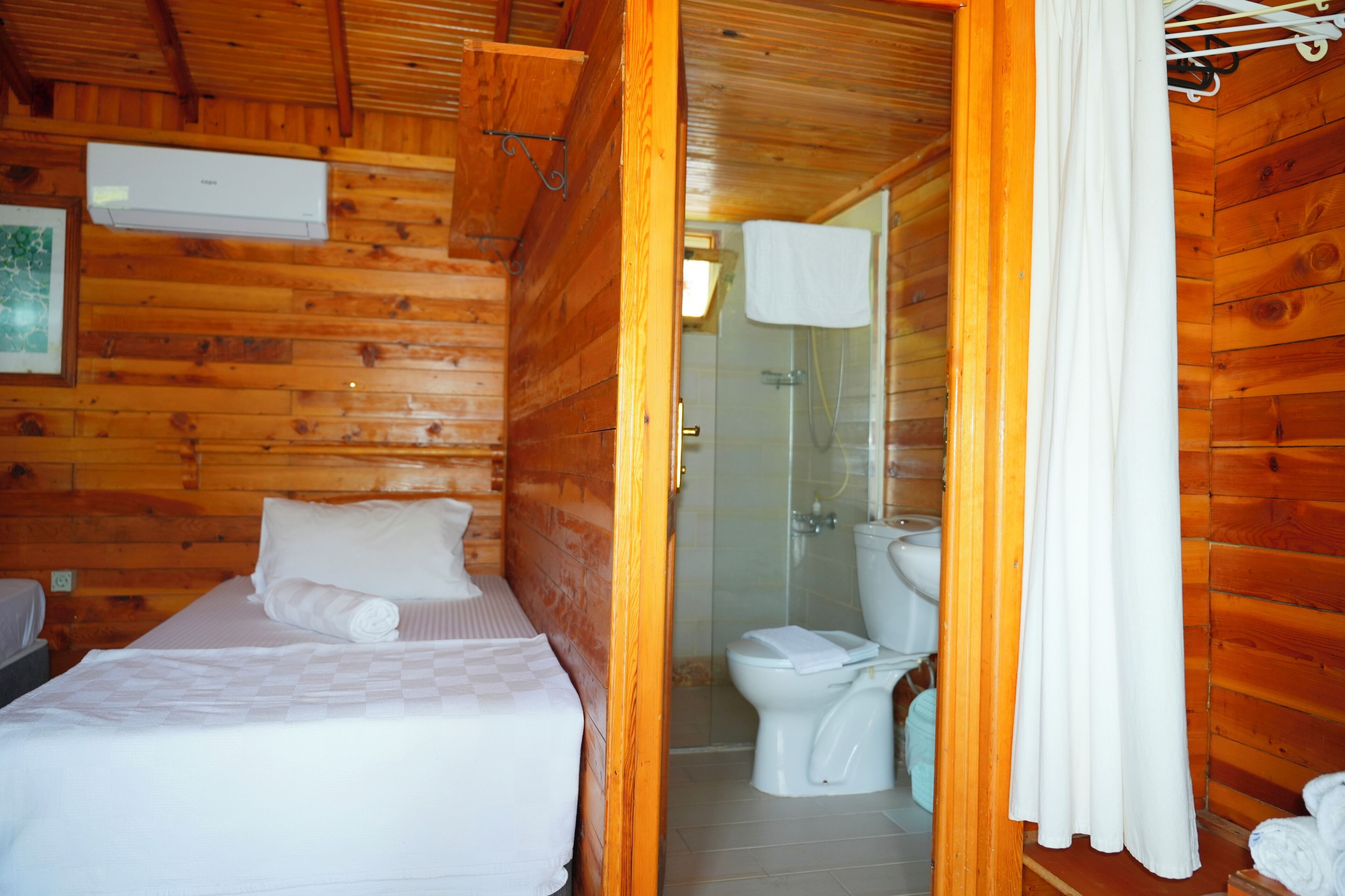 A wooden cabin room with a bed, a toilet, and a shower area.