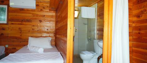 A wooden cabin room with a bed, a toilet, and a shower area.