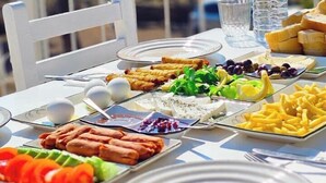 Et bord dækket udendørs med forskelligt mad, en vandflaske og et glas.