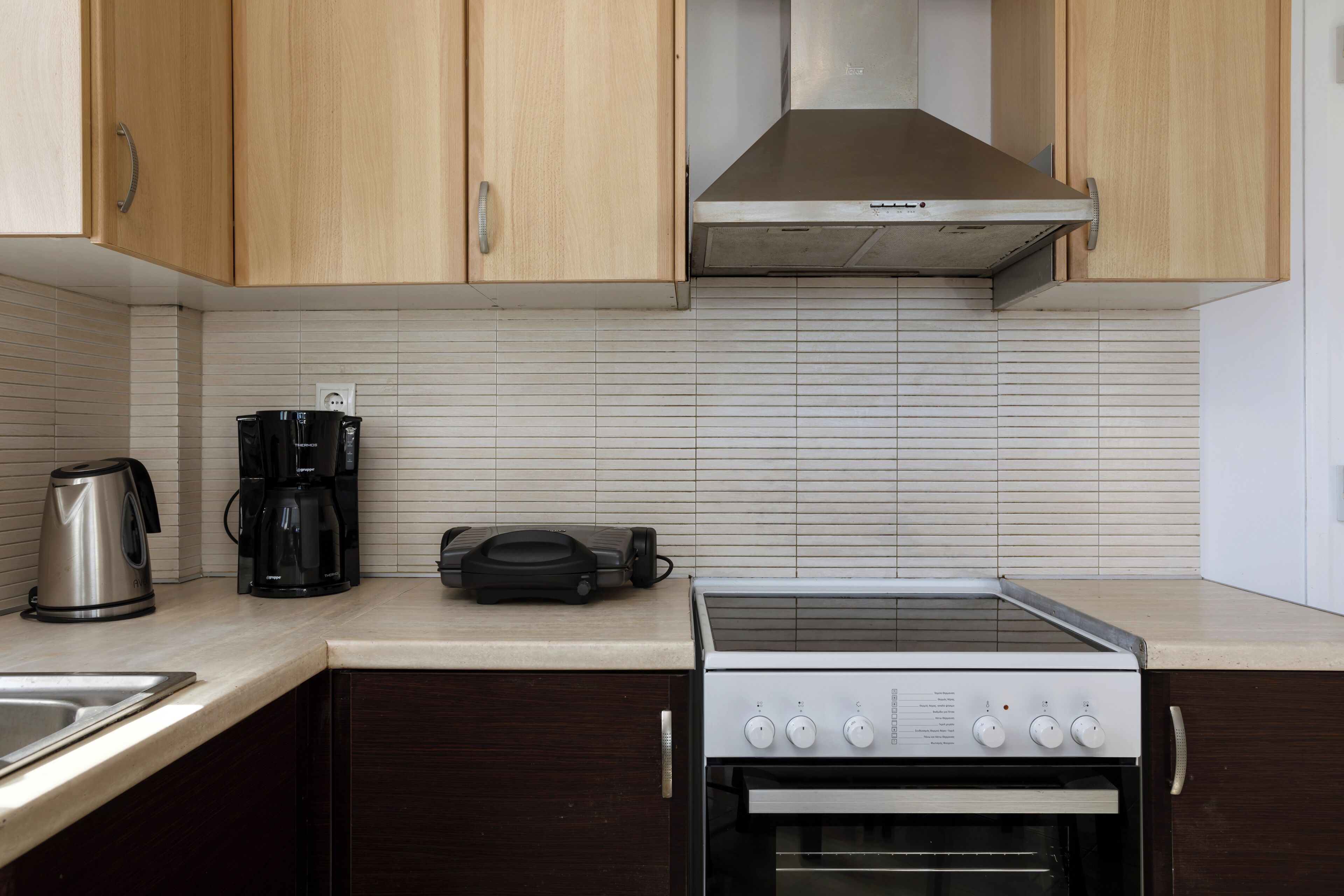 Una cucina con mobili in legno, una cappa aspirante in acciaio inox, una macchina da caffè e un forno.