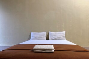 Un letto con biancheria bianca e una coperta marrone, due cuscini bianchi e un asciugamano piegato sul letto.