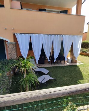 Un patio al aire libre con una zona de estar cubierta, un muro de piedra y una pequeña palmera.