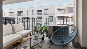 Ein Balkon mit einer Couch, einem Sessel, einem kleinen Tisch mit Blumenvase und einer Klimaanlage.