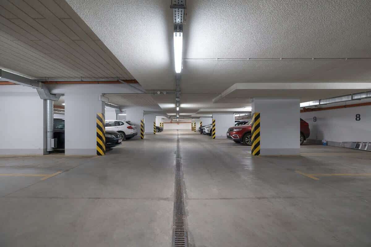 An underground parking garage with concrete floors, white walls, and yellow and black striped pillars.