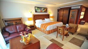 A hotel room with a large bed, a leather sofa, a wooden coffee table, and a small armchair. - Hôtel Abbasside Palace - Palm Beach (Algiers)