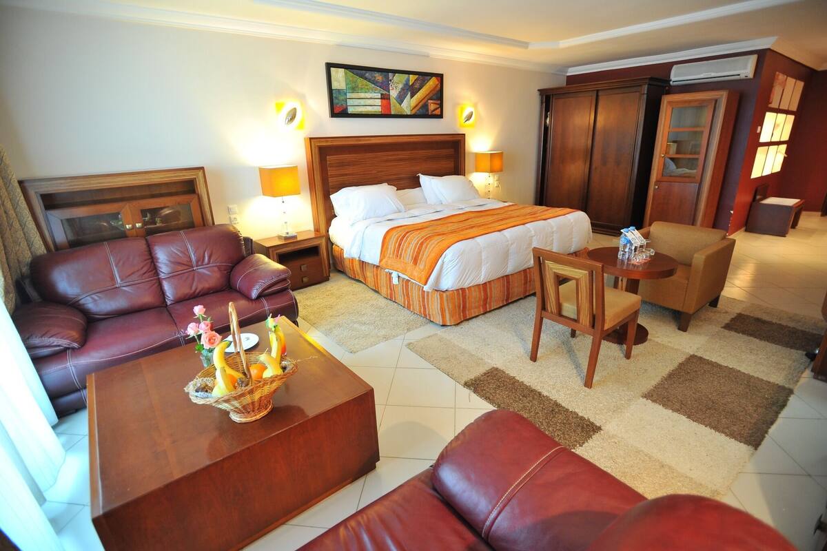 A hotel room with a large bed, a leather sofa, a wooden coffee table, and a small armchair.
