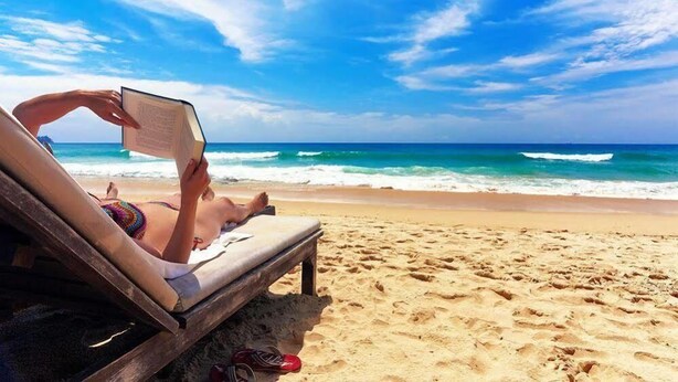 A person lying on a beach chair reading a book, with a wooden bench and sandals nearby. - Hôtel Abbasside Palace - Palm Beach (Algiers)