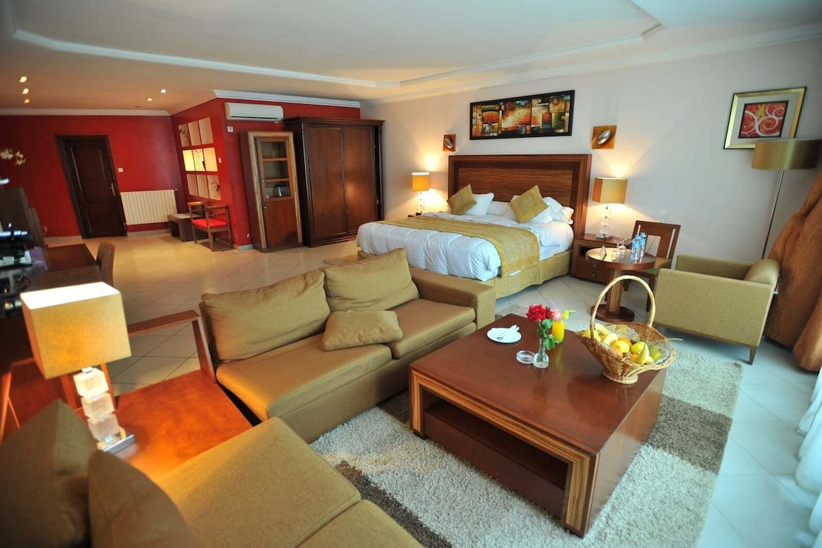 A hotel room with a bed, a sofa, a coffee table, a dining table, and a cabinet.