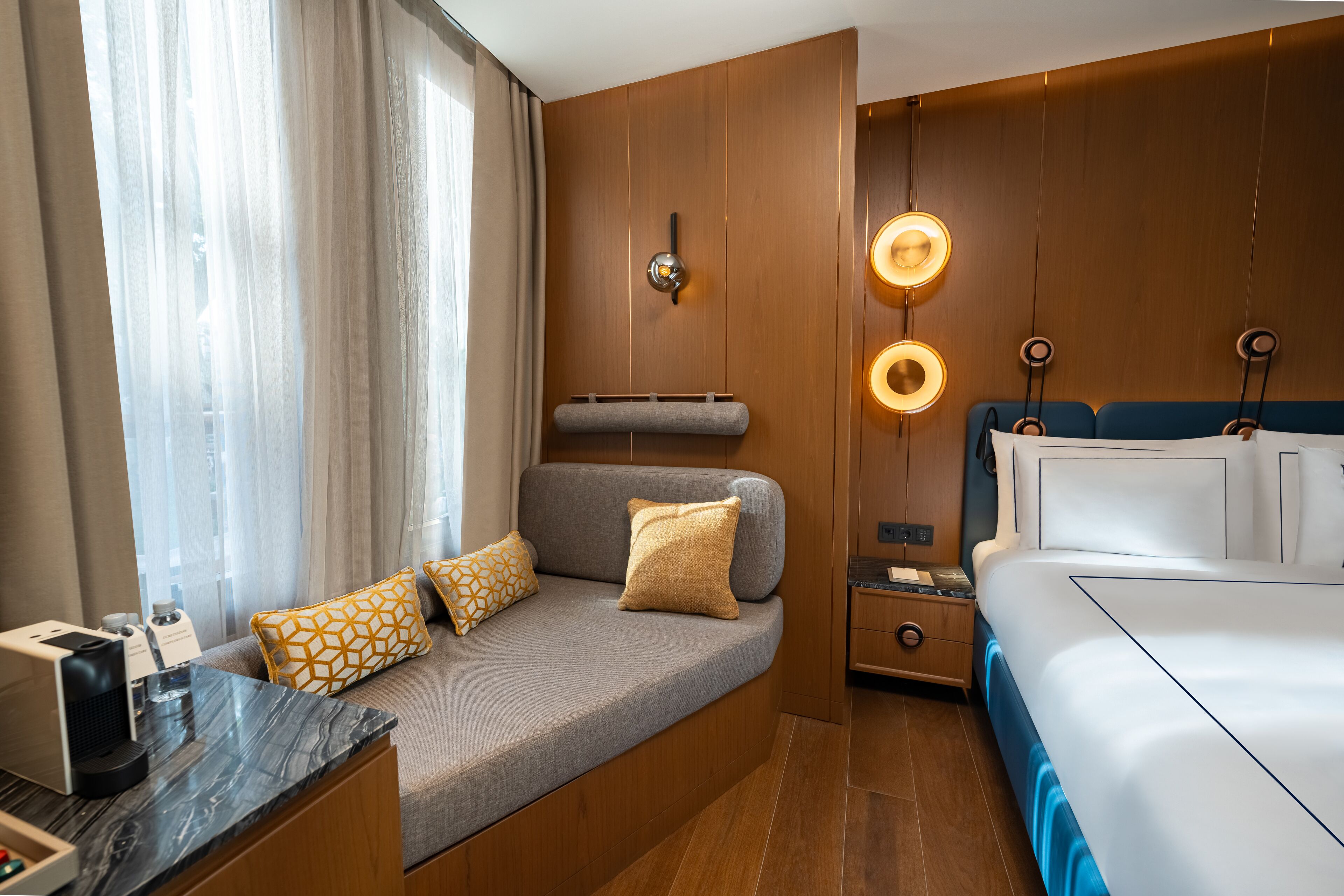 Una habitación de hotel moderna con sofá, cama, mesita de noche y escritorio con cafetera.