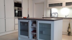 Una cocina moderna con armarios blancos, horno integrado e isla central con espacio de almacenamiento.
