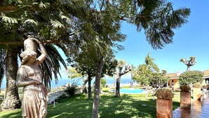 Une statue dans un jardin, avec une piscine et une vue sur la mer.