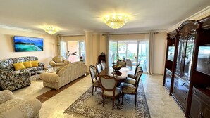 Un salón amplio con una gran mesa de comedor, asientos cómodos, un televisor y vistas a través de puertas de vidrio.