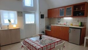 A compact kitchen with a dining table, chairs, and basic appliances. - Santorini Cave Escape in Oia w Patio (Santorini)