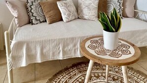 A cozy living room with a beige sofa, patterned cushions, a round wooden coffee table, and a decorative rug. - Santorini Cave Escape in Oia w Patio (Santorini)