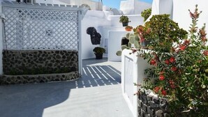 A white-walled building with a stone wall and a lattice fence. - Santorini Cave Escape in Oia w Patio (Santorini)