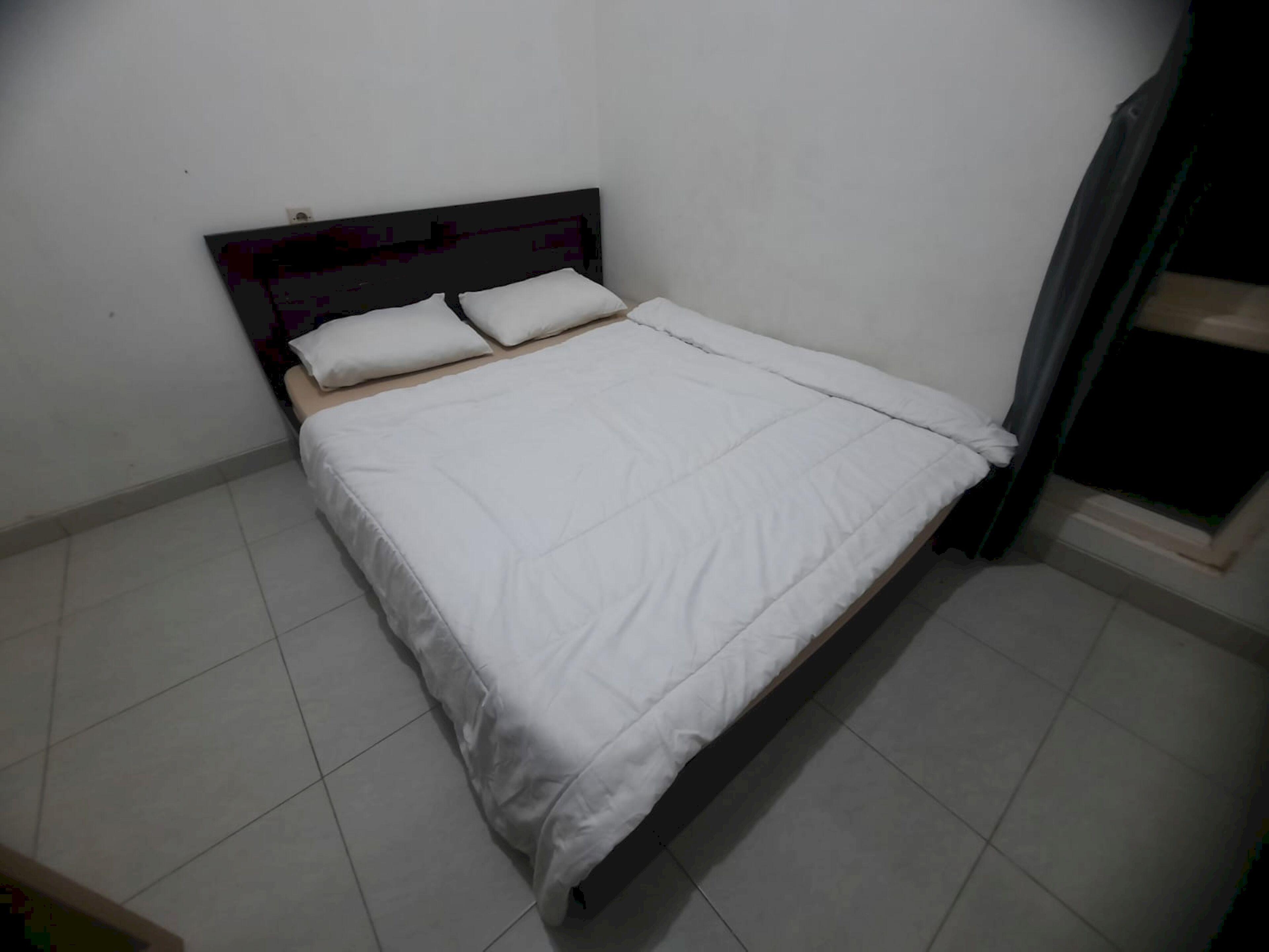 A single bed with white bedding in a room with plain walls and tiled flooring.