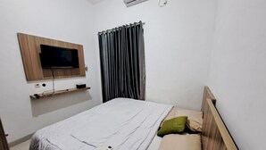 A bedroom with a bed, a mounted TV, a shelf, and a window with curtains. - OYO 93870 Damai Guest House Cirebon (West Cirebon)
