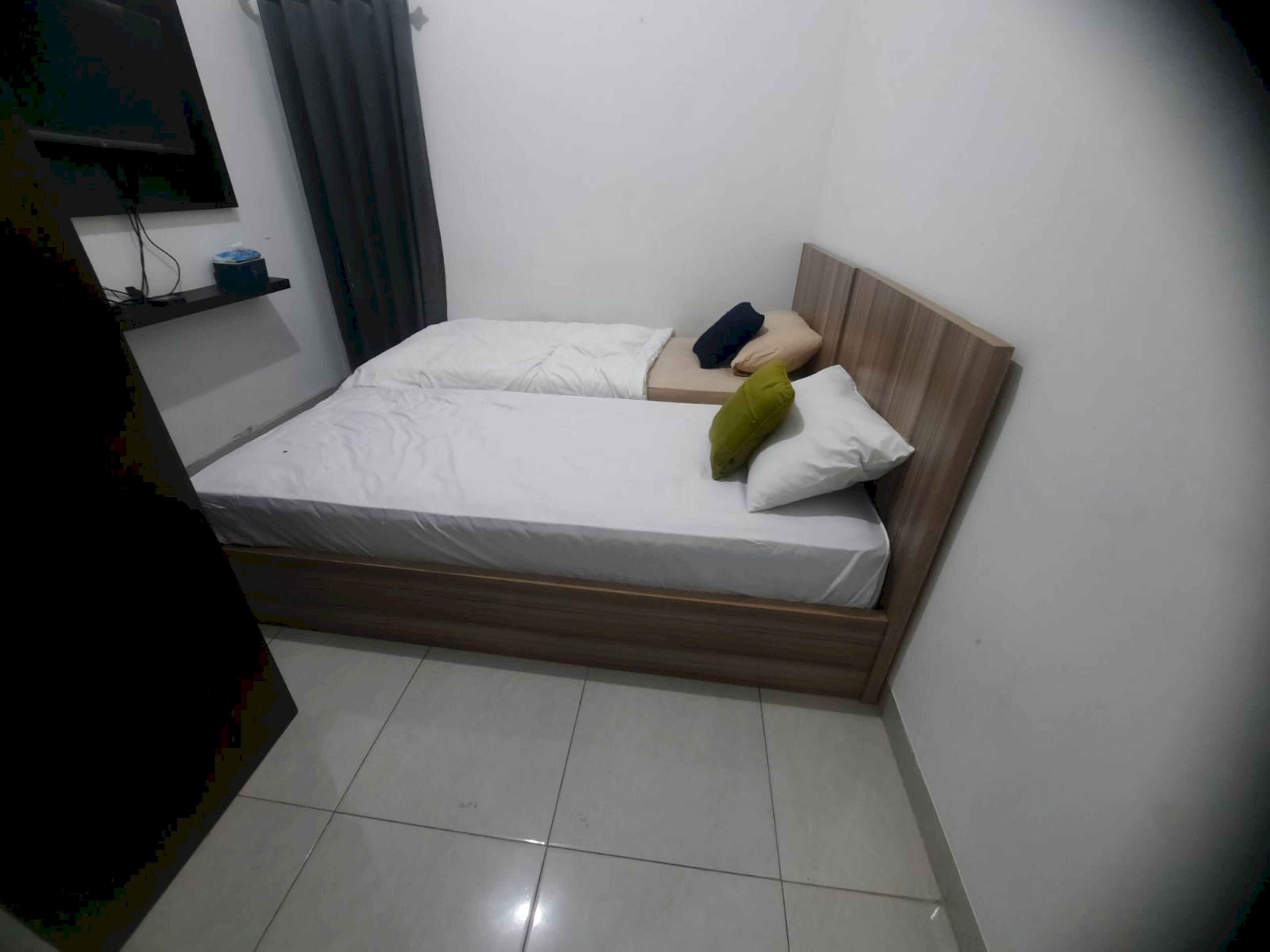 Ein kleines, sauberes Zimmer mit einem Einzelbett, einem Nachttisch und einem an der Wand befestigten Regal.