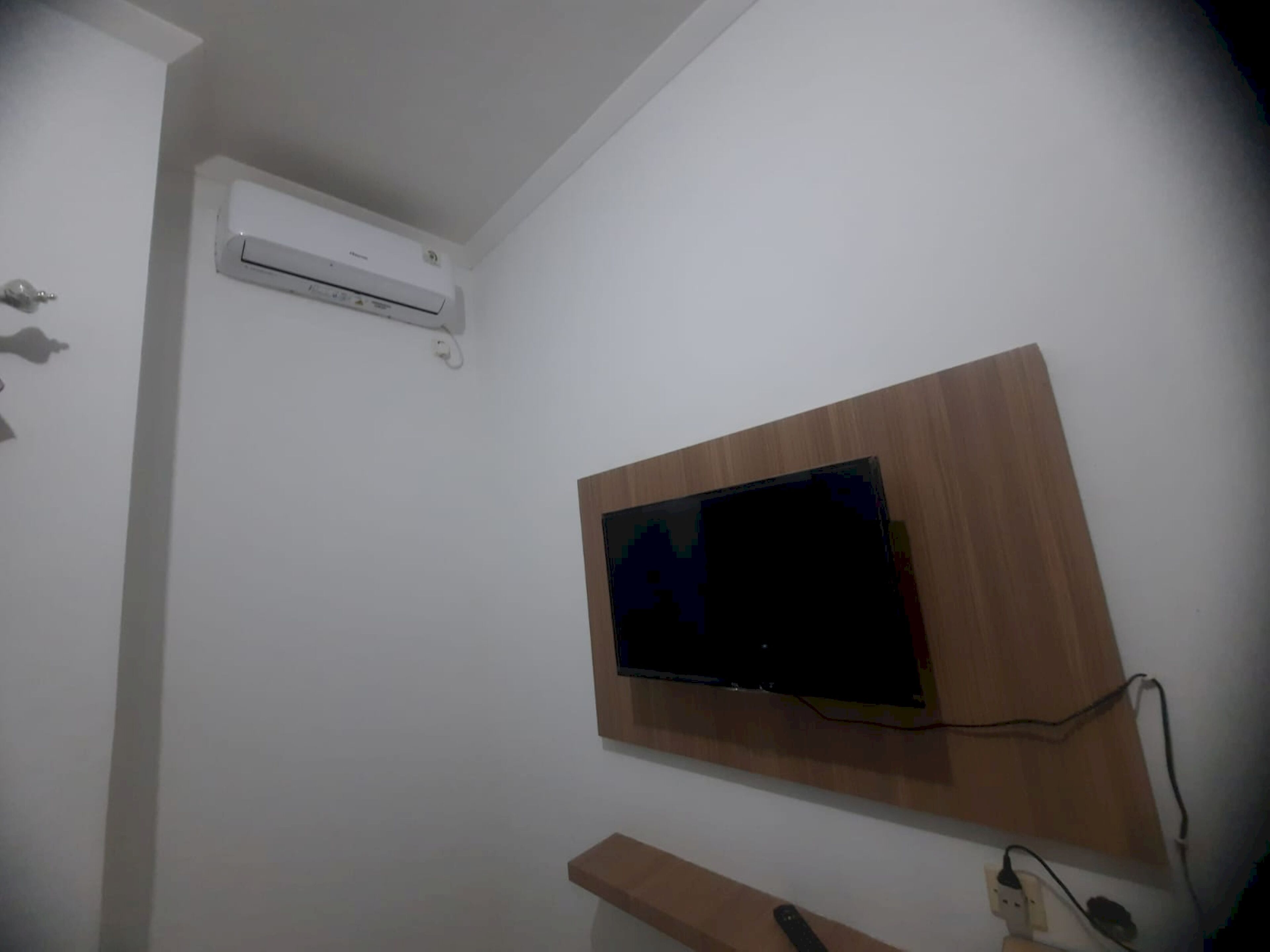 Una habitación con un televisor de pantalla plana montado en un panel de madera, un equipo de aire acondicionado en la pared y un enchufe con cable.