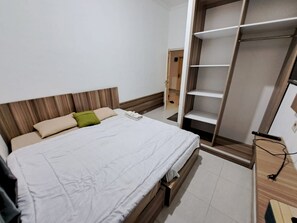 A bedroom with a bed, a wooden headboard, a wardrobe, and a bedside table with a remote control. - OYO 93870 Damai Guest House Cirebon (West Cirebon)