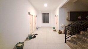 A hallway with a staircase on the right, a window with curtains, and a trash bin on the left. - OYO 93870 Damai Guest House Cirebon (West Cirebon)
