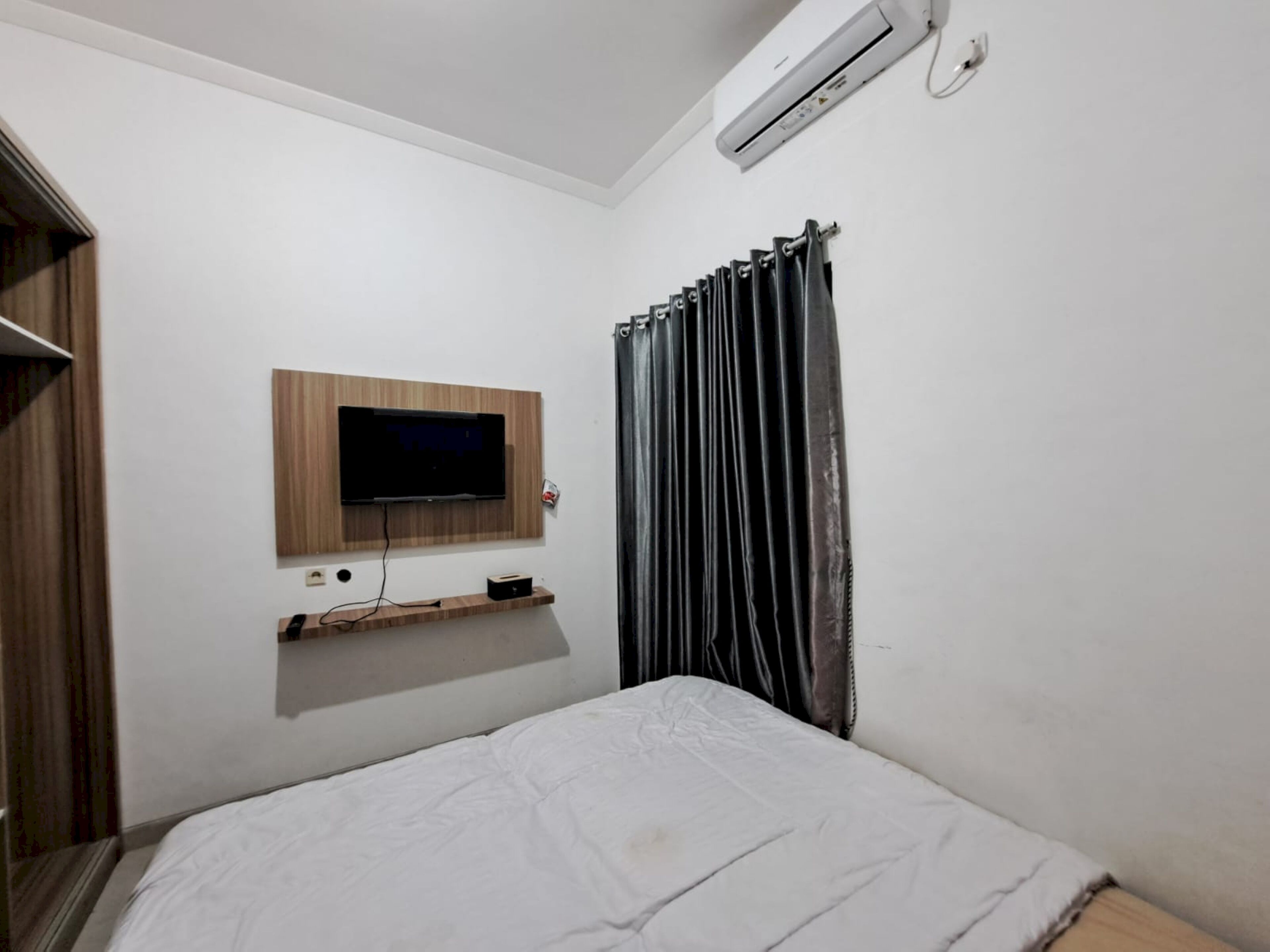 A bedroom with a bed, a mounted TV, a shelf, and a curtain.