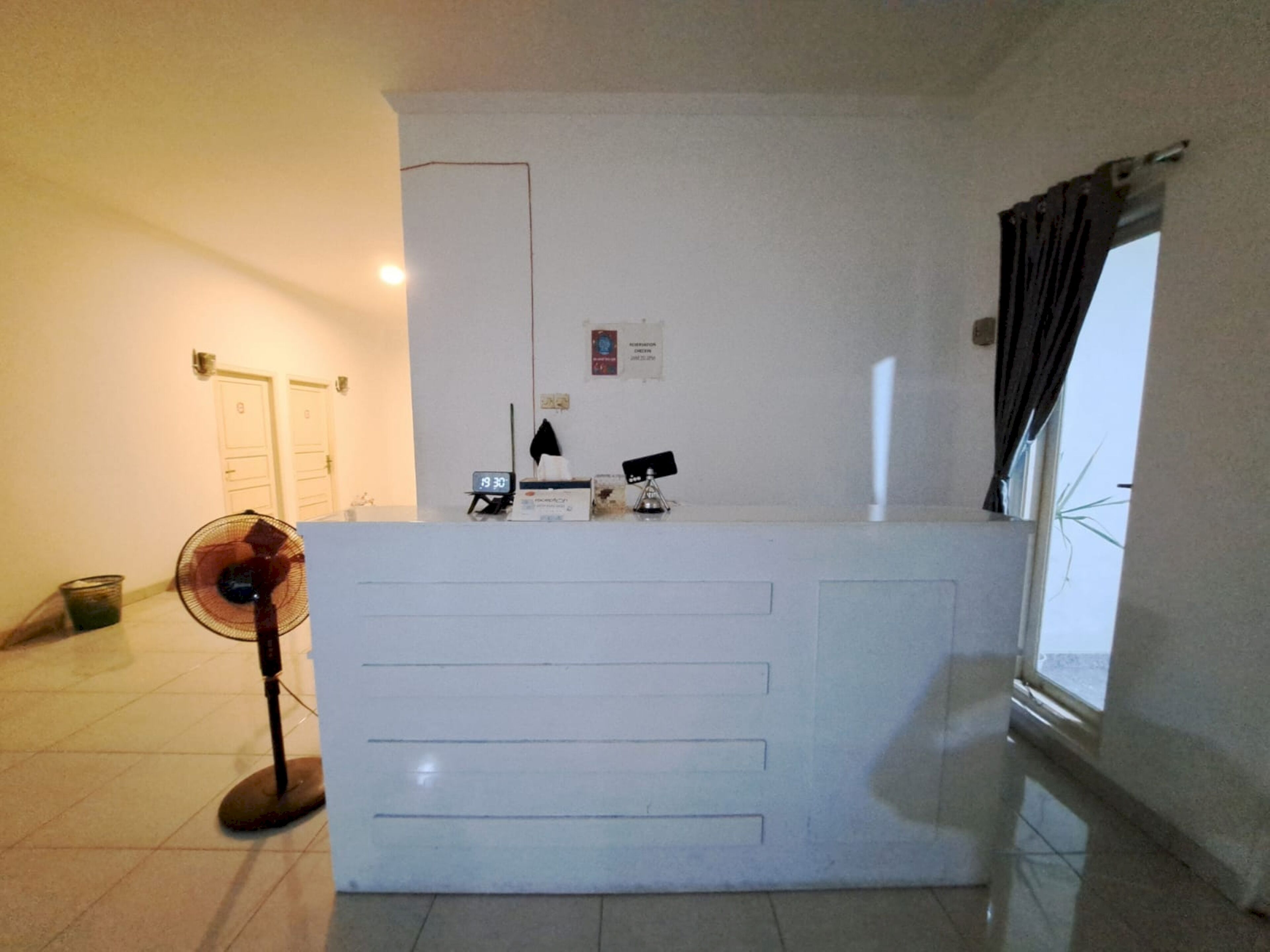 A reception desk with a clock, a fan, and a window with curtains.