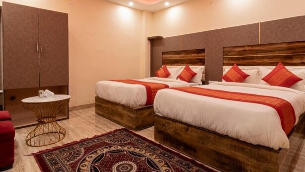 Habitación de hotel con dos camas, cabecera de madera, alfombra estampada en rojo y blanco, una mesita redonda y un armario.