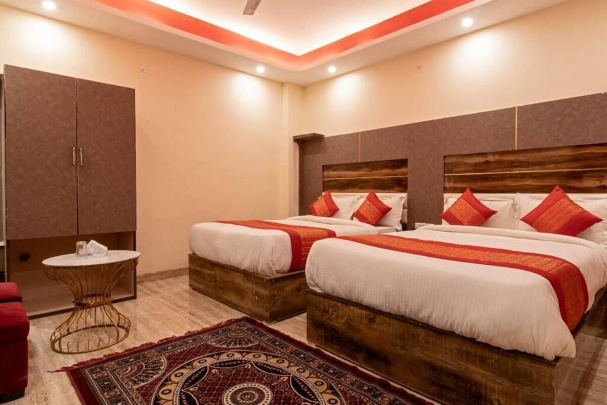 A hotel room with two beds, a wooden headboard, a red and white patterned rug, a small round table, and a wardrobe.