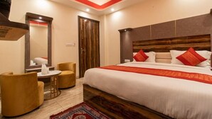 Habitación de hotel con una cama grande, cabecera de madera, una mesa redonda con sillas y un espejo.