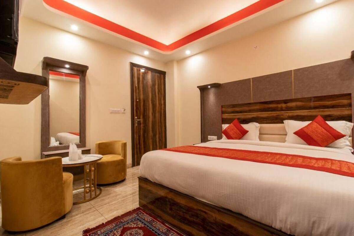 A hotel room with a large bed, a wooden headboard, a round table with chairs, and a mirror.