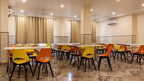 Un salón de conferencias con varias mesas y sillas, unidades de aire acondicionado y cortinas.
