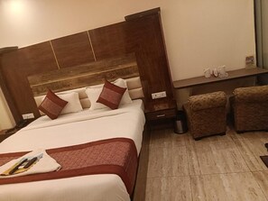 A hotel room with a large bed, a wooden headboard, two armchairs, a small table with a telephone and a cup, and a trash bin. - Hotel Dev Residency By GRB (New Delhi)