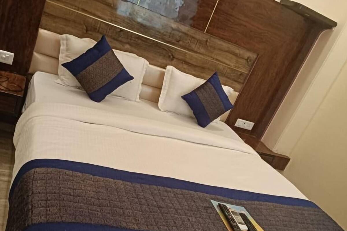 A neatly made bed with white and blue bedding, a wooden headboard, and a remote control on the bed.