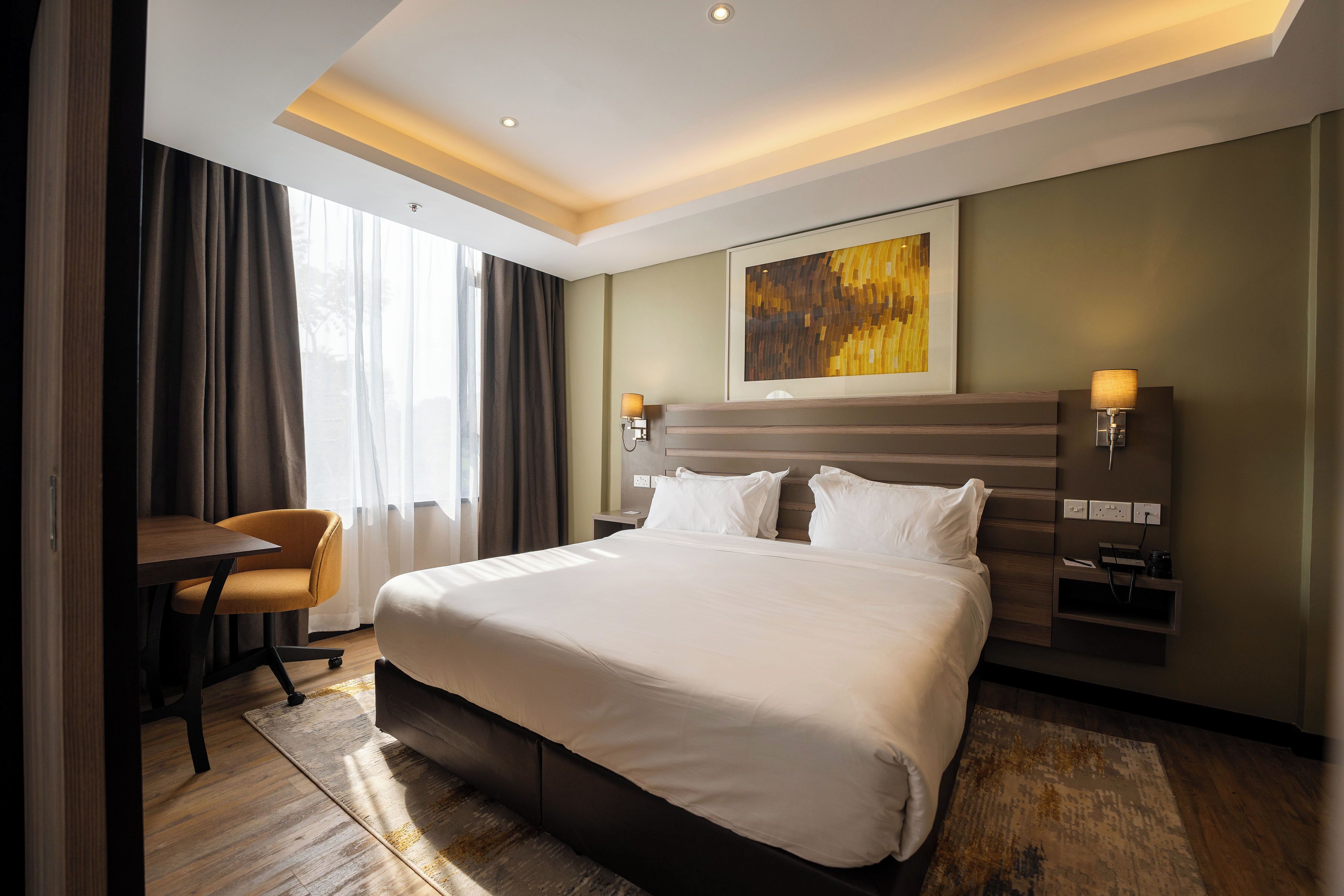 Ein Hotelzimmer mit einem großen Bett, einem Schreibtisch, einem Stuhl und einem Bild an der Wand.