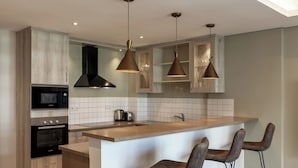 Une cuisine moderne dotée d’un îlot central, d’appareils électroménagers intégrés et de luminaires suspendus.